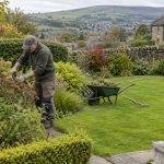Gardener tending a mixed border in a stone-walled West Yorkshire garden.