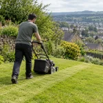 Gardener mowing a sloping lawn beside a stone wall in Keighley.